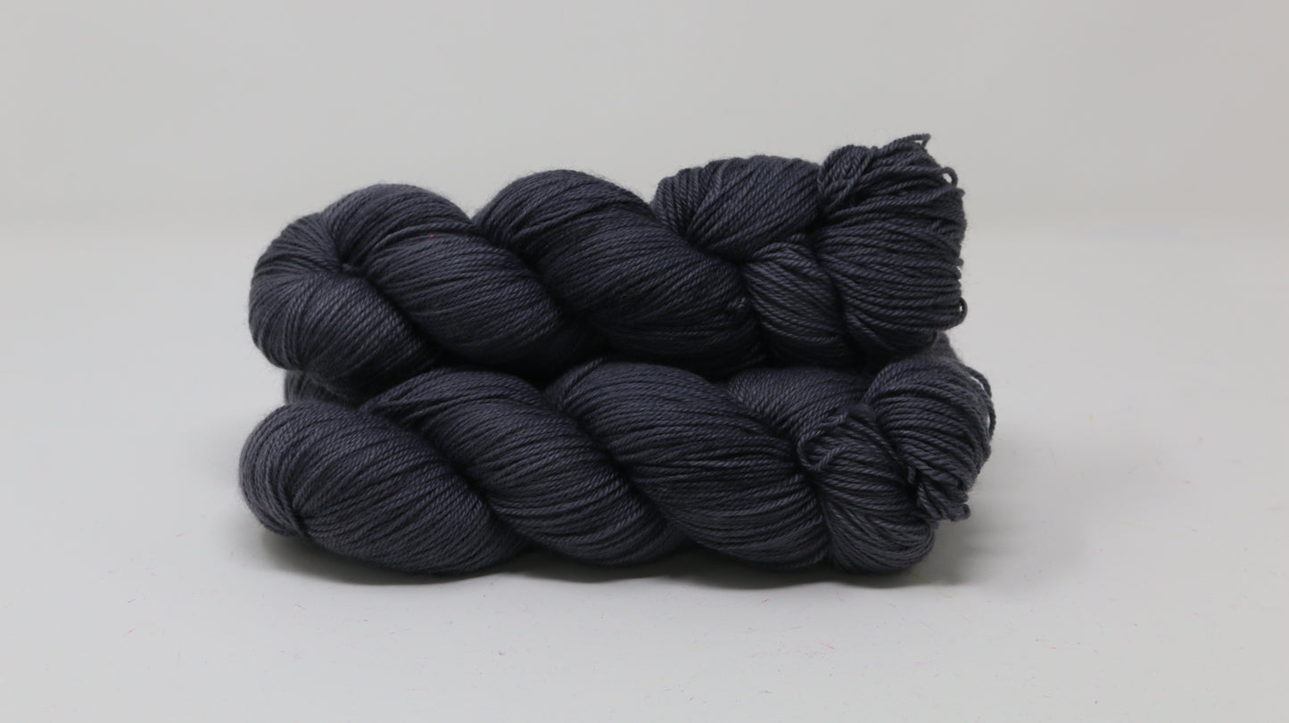 3 skeins of dark grey yarn on a white surface and background