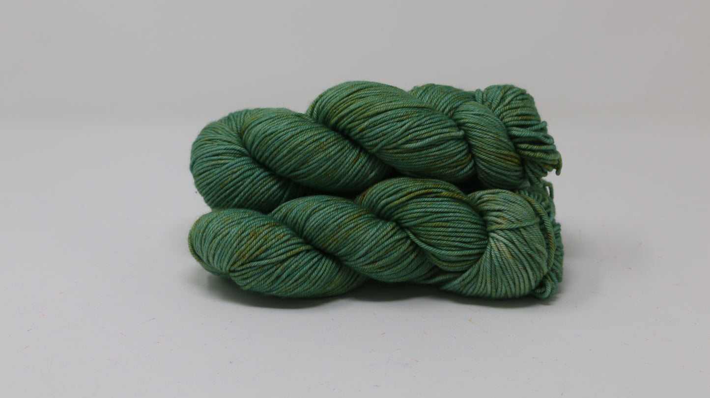 3 skeins of green yarn speckled with gold accents displayed on a white surface and background
