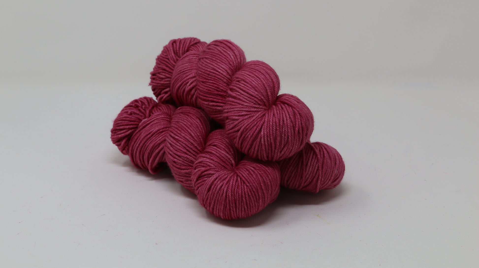 3 skeins of dark pink yarn on a white surface and background