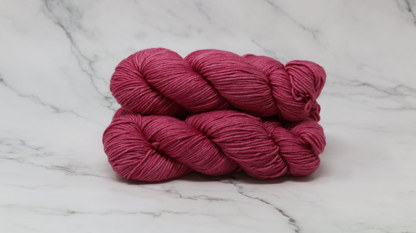 3 skeins of dark pink yarn on a white marble surface and background