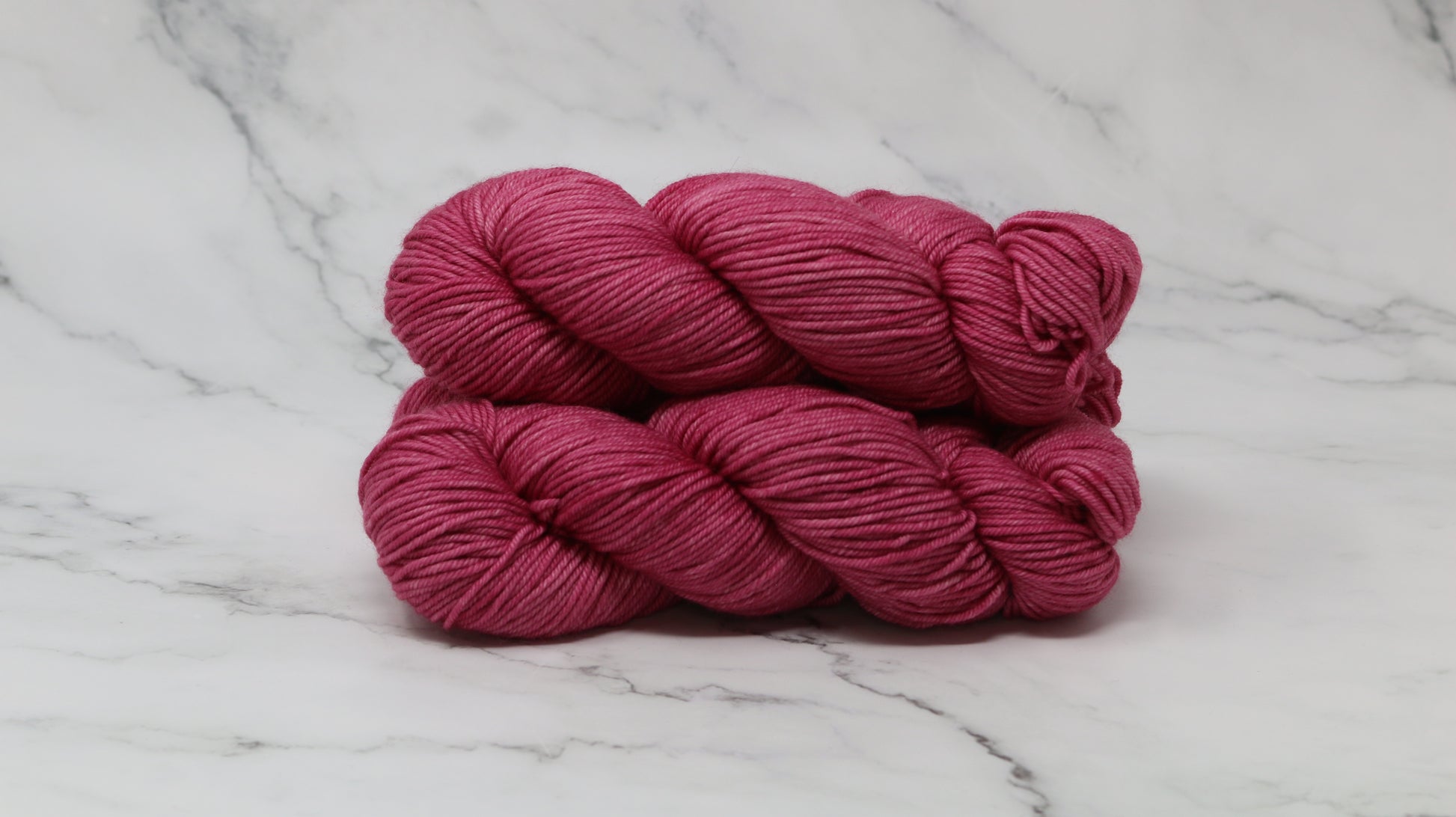 3 skeins of dark pink yarn on a white marble surface and background