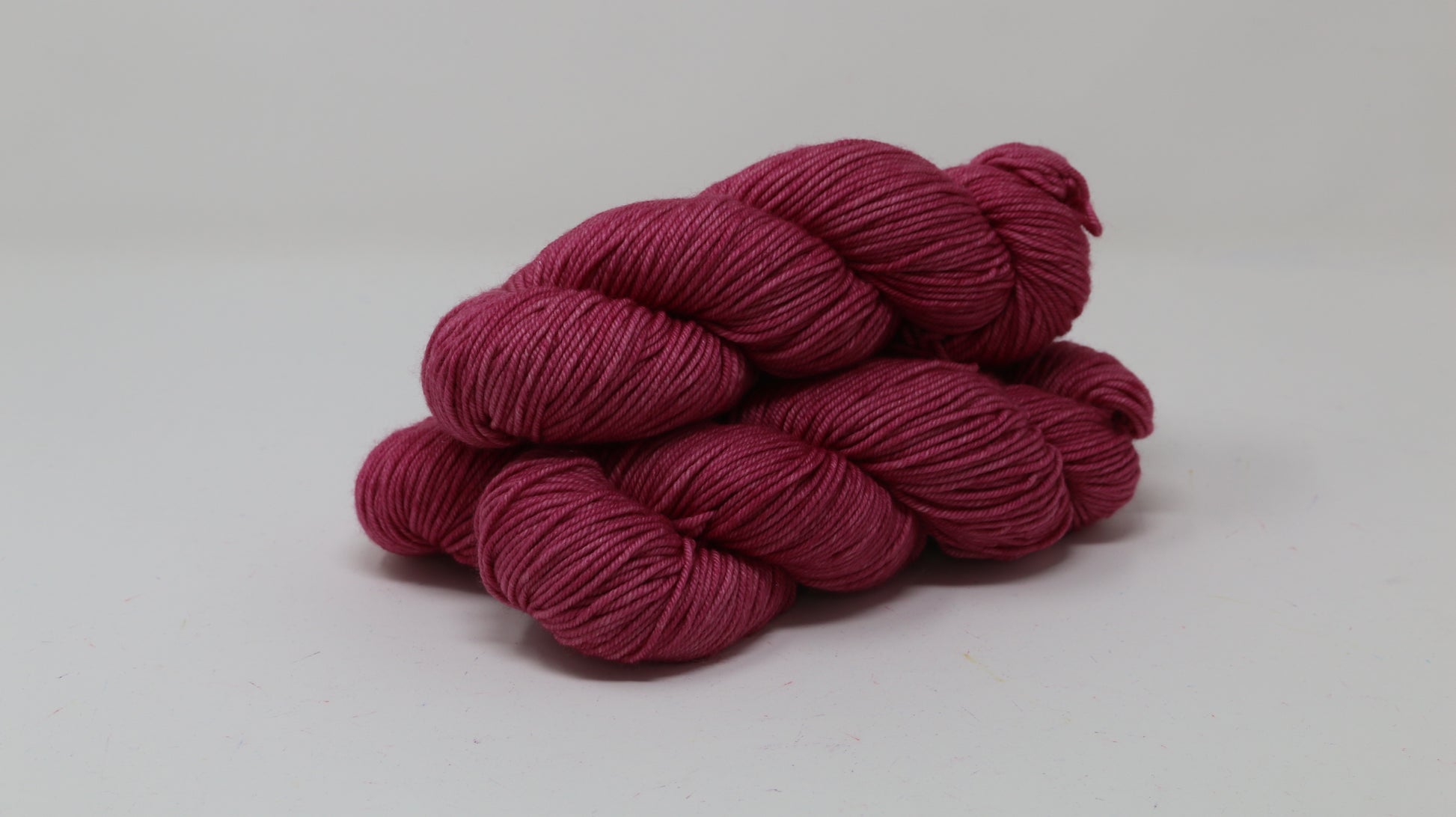 3 skeins of dark pink yarn on a white surface and background