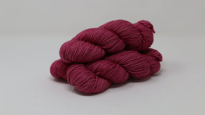 3 skeins of dark pink yarn on a white surface and background