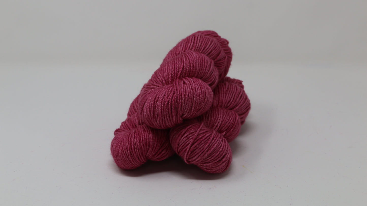 3 skeins of dark pink yarn on a white surface and background