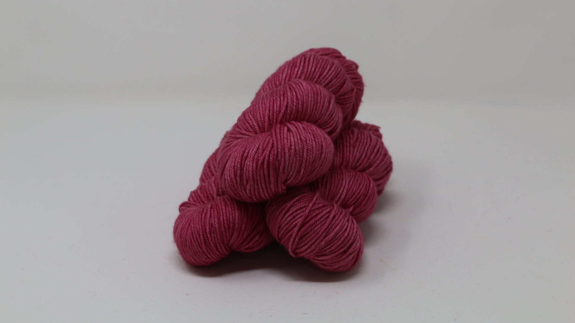 3 skeins of dark pink yarn on a white surface and background