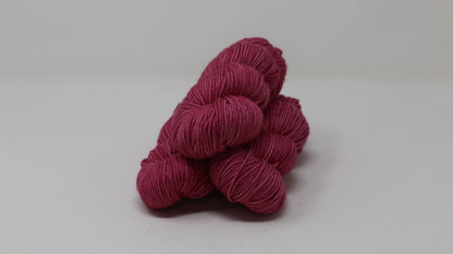 3 skeins of dark pink yarn on a white surface and background