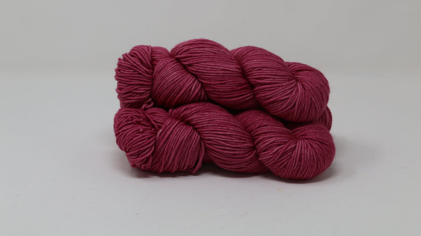 3 skeins of dark pink yarn on a white surface and background