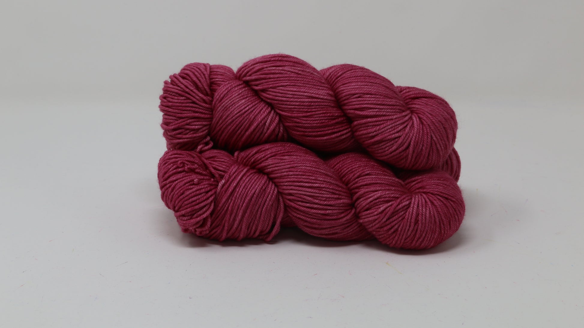 3 skeins of dark pink yarn on a white surface and background