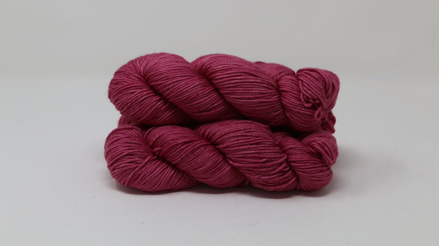 3 skeins of dark pink yarn on a white surface and background