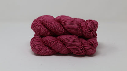 3 skeins of dark pink yarn on a white surface and background