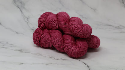 3 skeins of dark pink yarn on a white marble surface and background