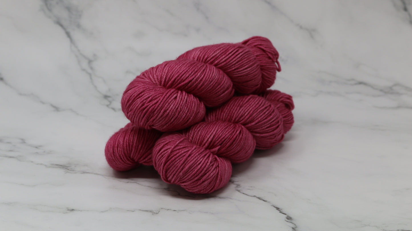 3 skeins of dark pink yarn on a white marble surface and background