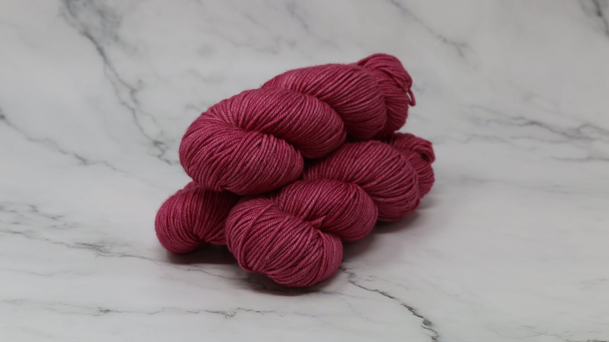 3 skeins of dark pink yarn on a white marble surface and background