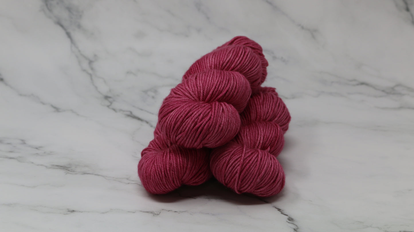 3 skeins of dark pink yarn on a white marble surface and background