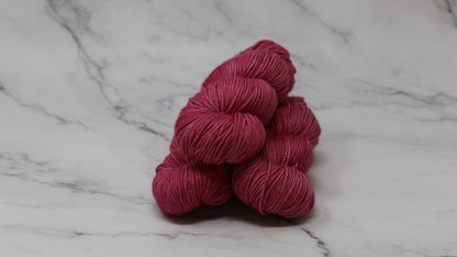 3 skeins of dark pink yarn on a white marble surface and background