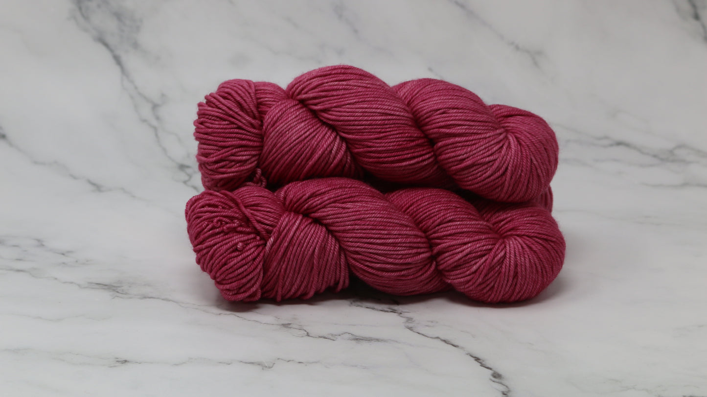 3 skeins of dark pink yarn on a white marble surface and background