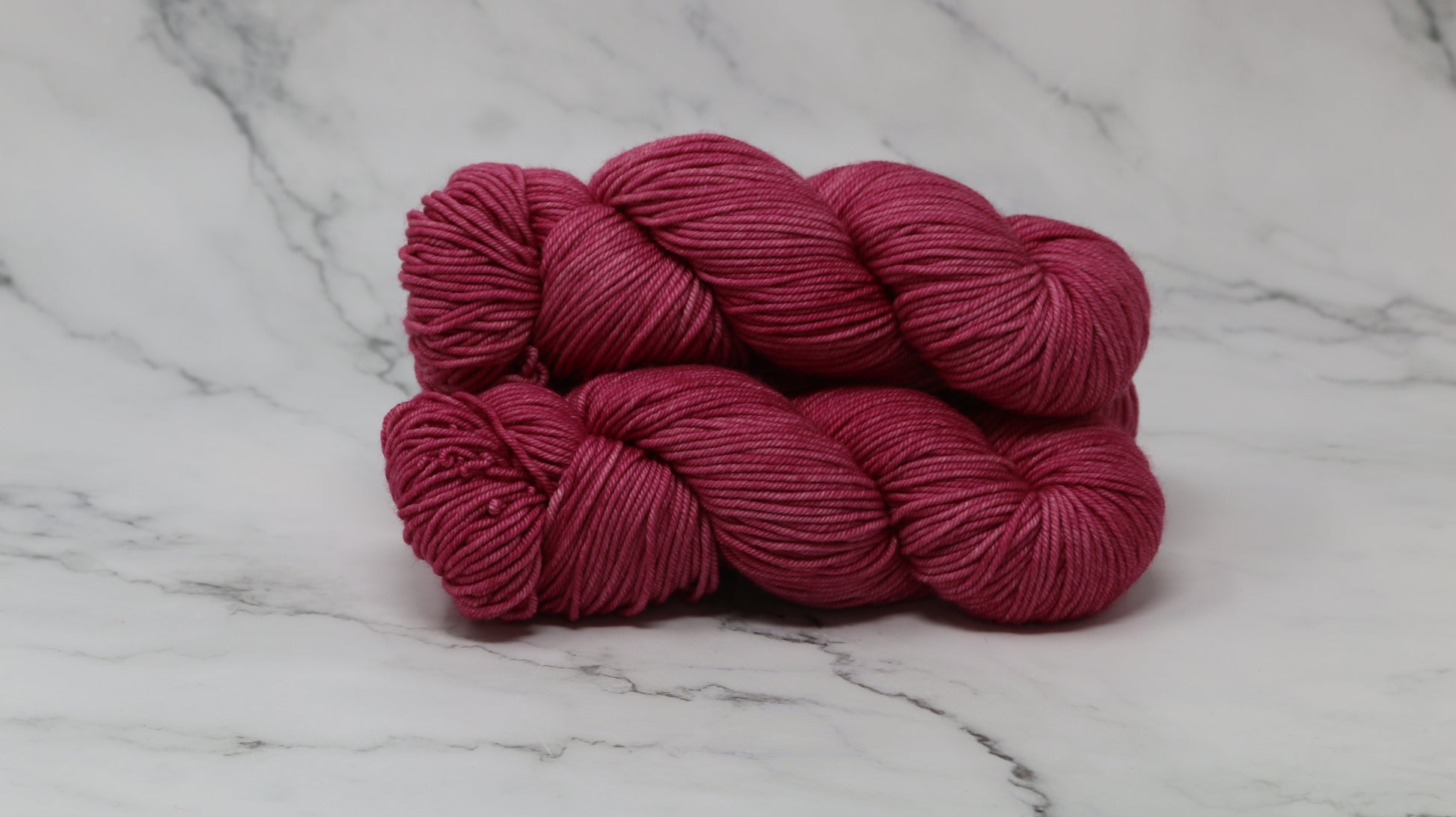3 skeins of dark pink yarn on a white marble surface and background