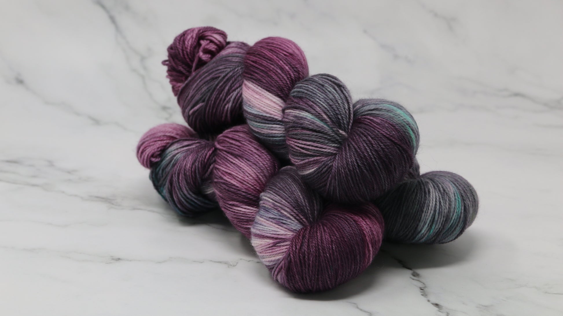 Three skeins of variegated yarn skeins in shades of purple, pink, green and dark gray