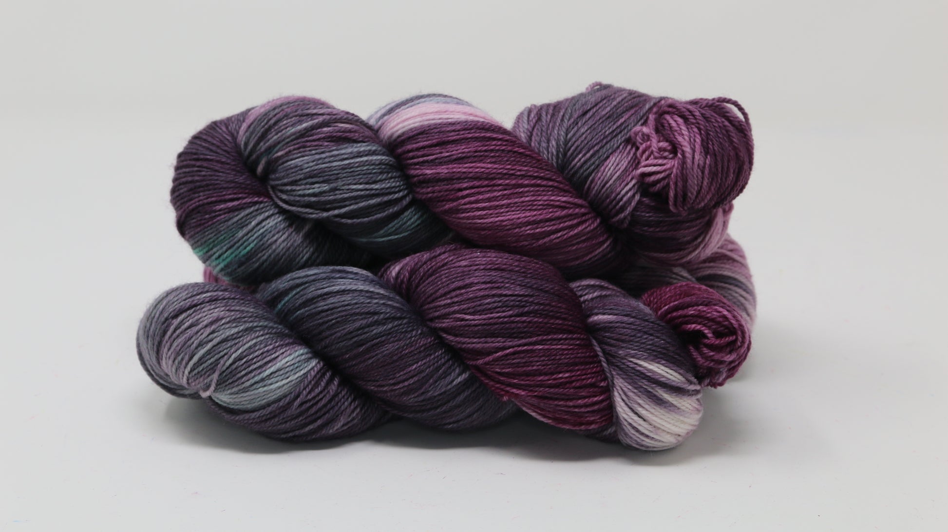 Three skeins of variegated yarn skeins in shades of purple, pink, green and dark gray