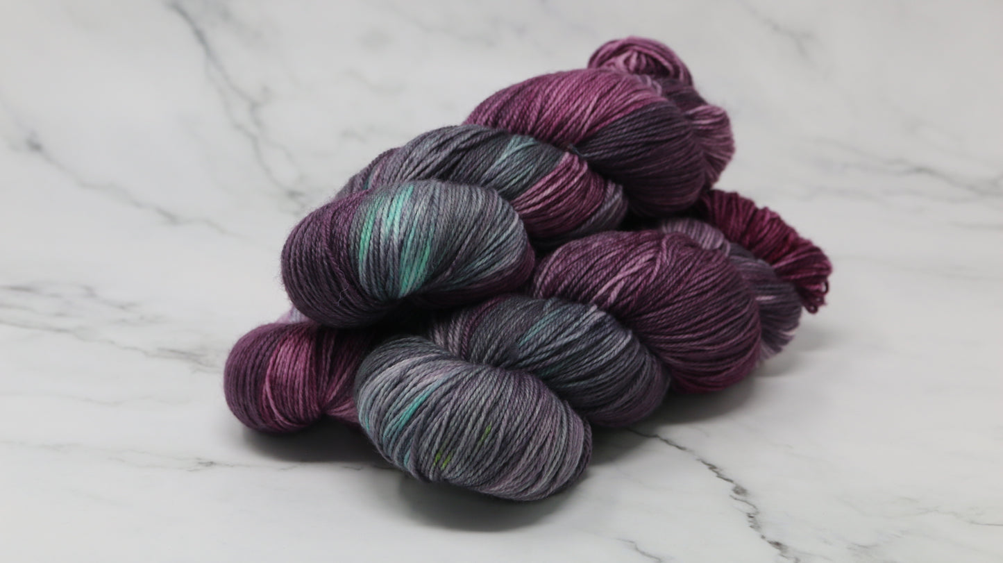 Three skeins of variegated yarn skeins in shades of purple, pink, green and dark gray