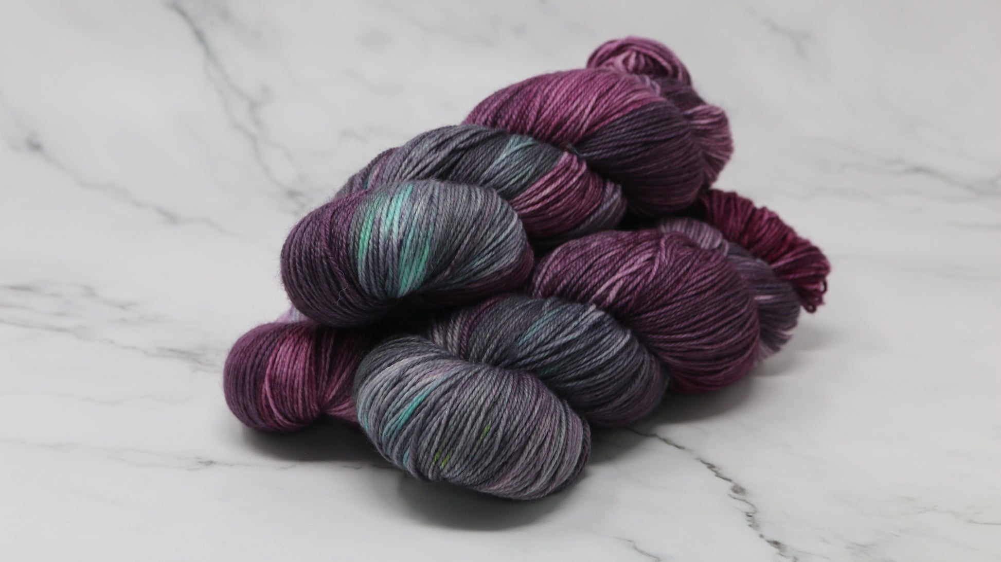 Three skeins of variegated yarn skeins in shades of purple, pink, green and dark gray