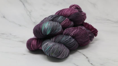 Three skeins of variegated yarn skeins in shades of purple, pink, green and dark gray