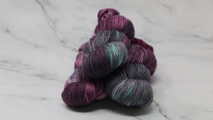 Three skeins of variegated yarn skeins in shades of purple, pink, green and dark gray