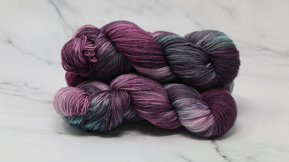Three skeins of variegated yarn skeins in shades of purple, pink, green and dark gray