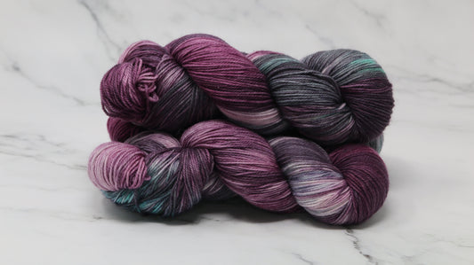 Three skeins of variegated yarn skeins in shades of purple, pink, green and dark gray