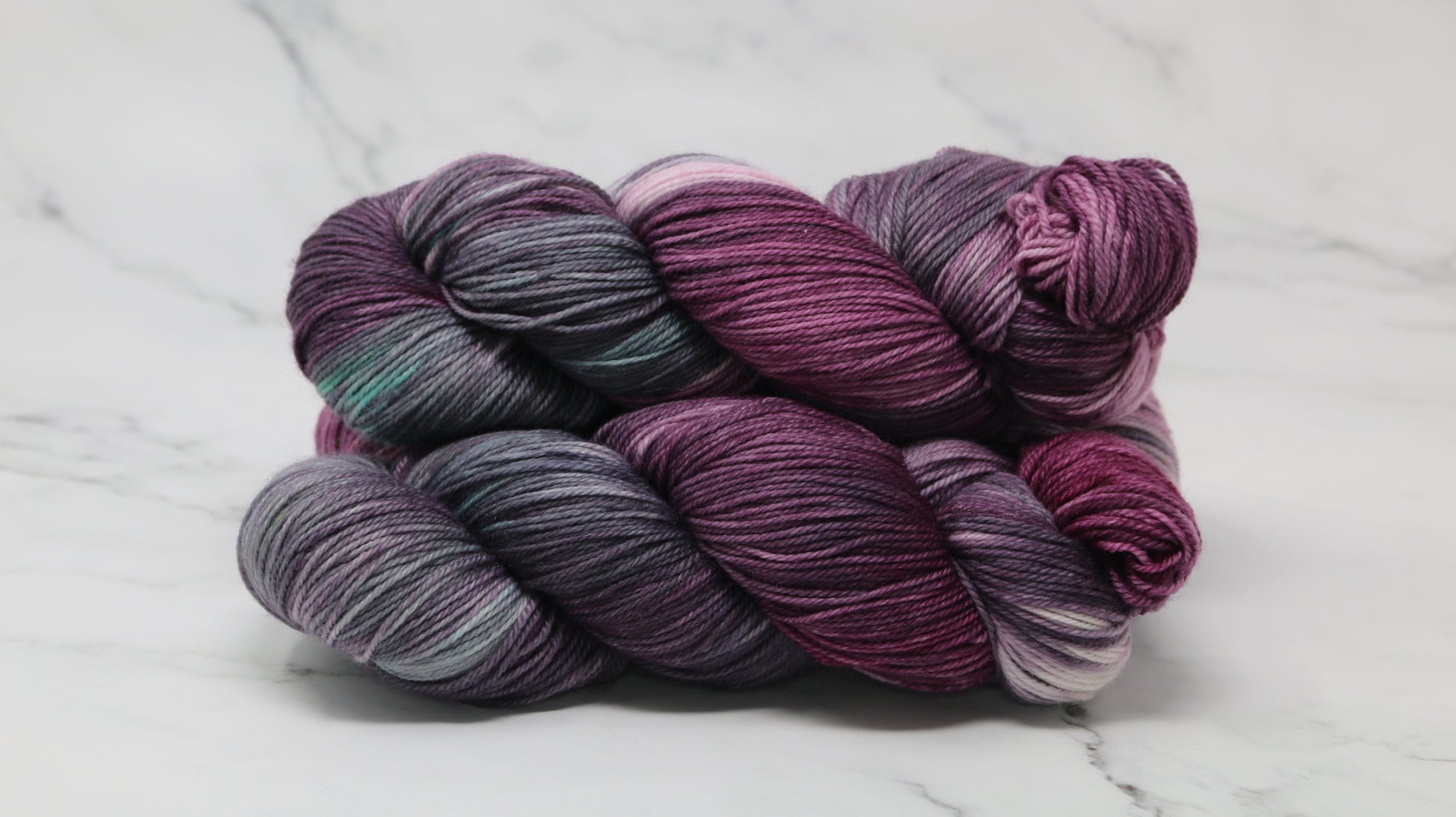 Three skeins of variegated yarn skeins in shades of purple, pink, green and dark gray