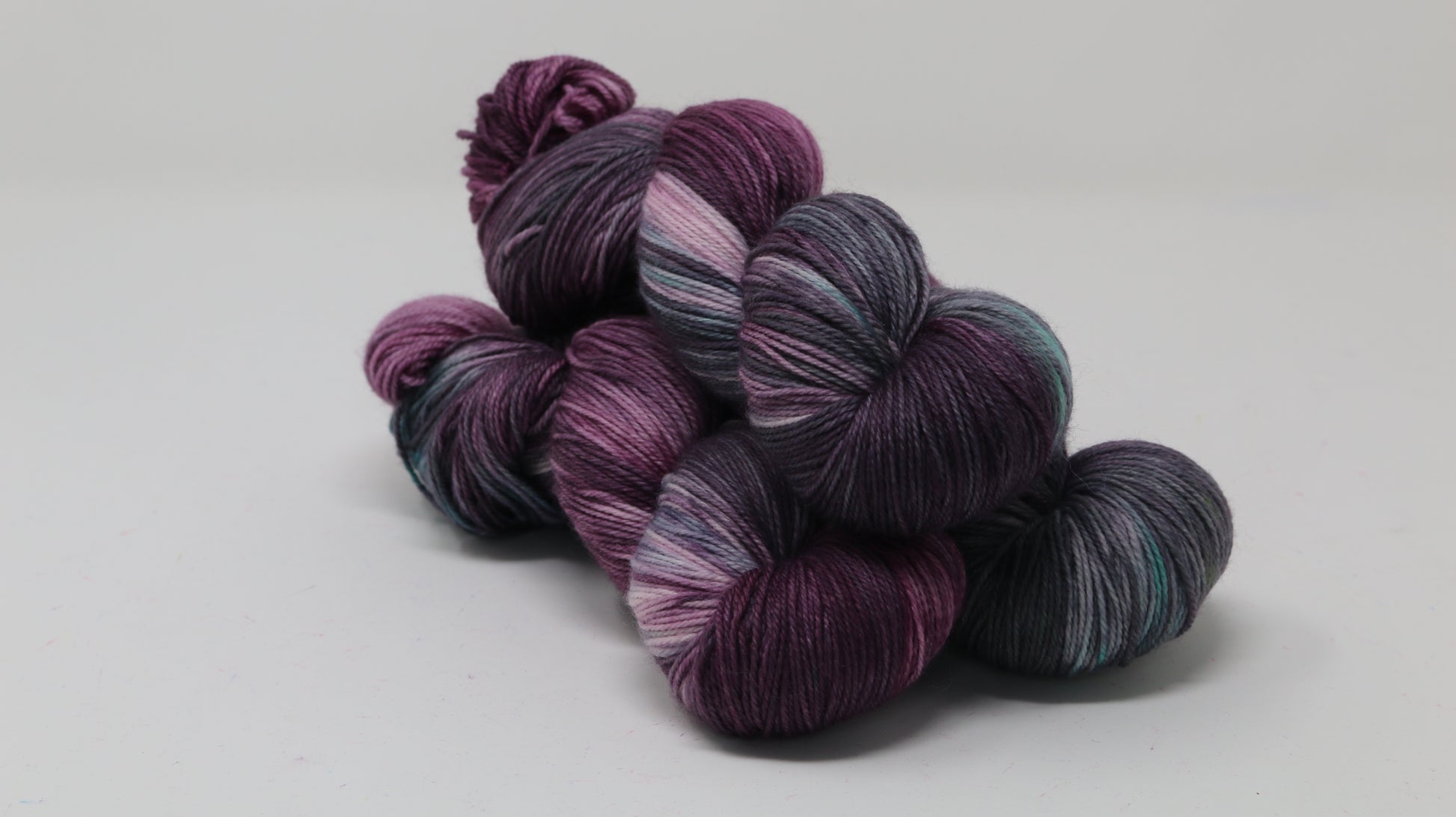 Three skeins of variegated yarn skeins in shades of purple, pink, green and dark gray