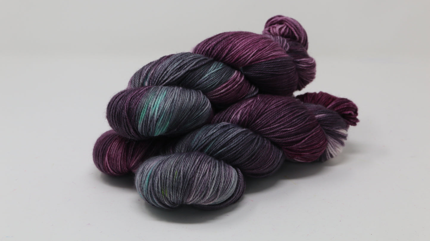 Three skeins of variegated yarn skeins in shades of purple, pink, green and dark gray
