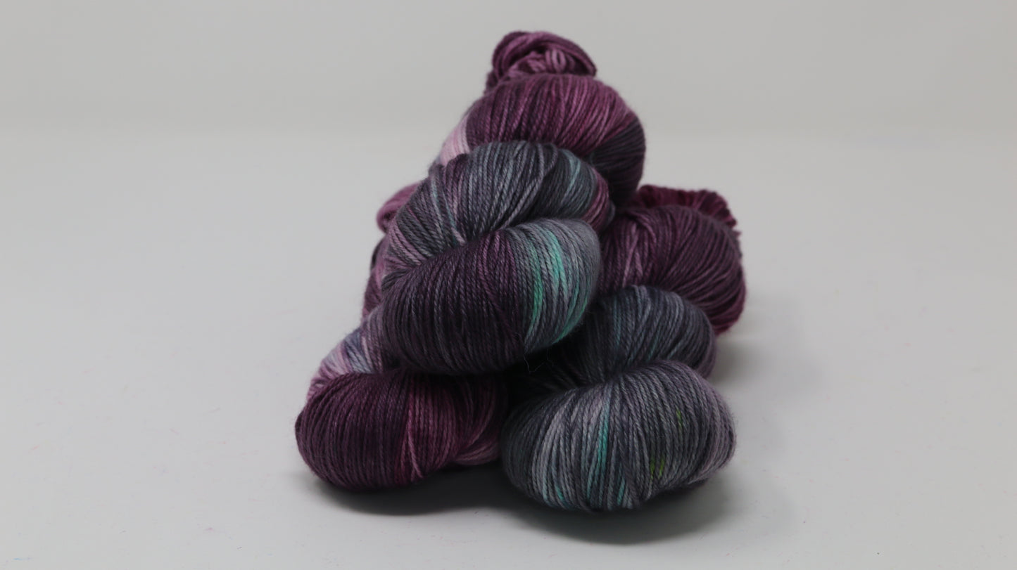 Three skeins of variegated yarn skeins in shades of purple, pink, green and dark gray