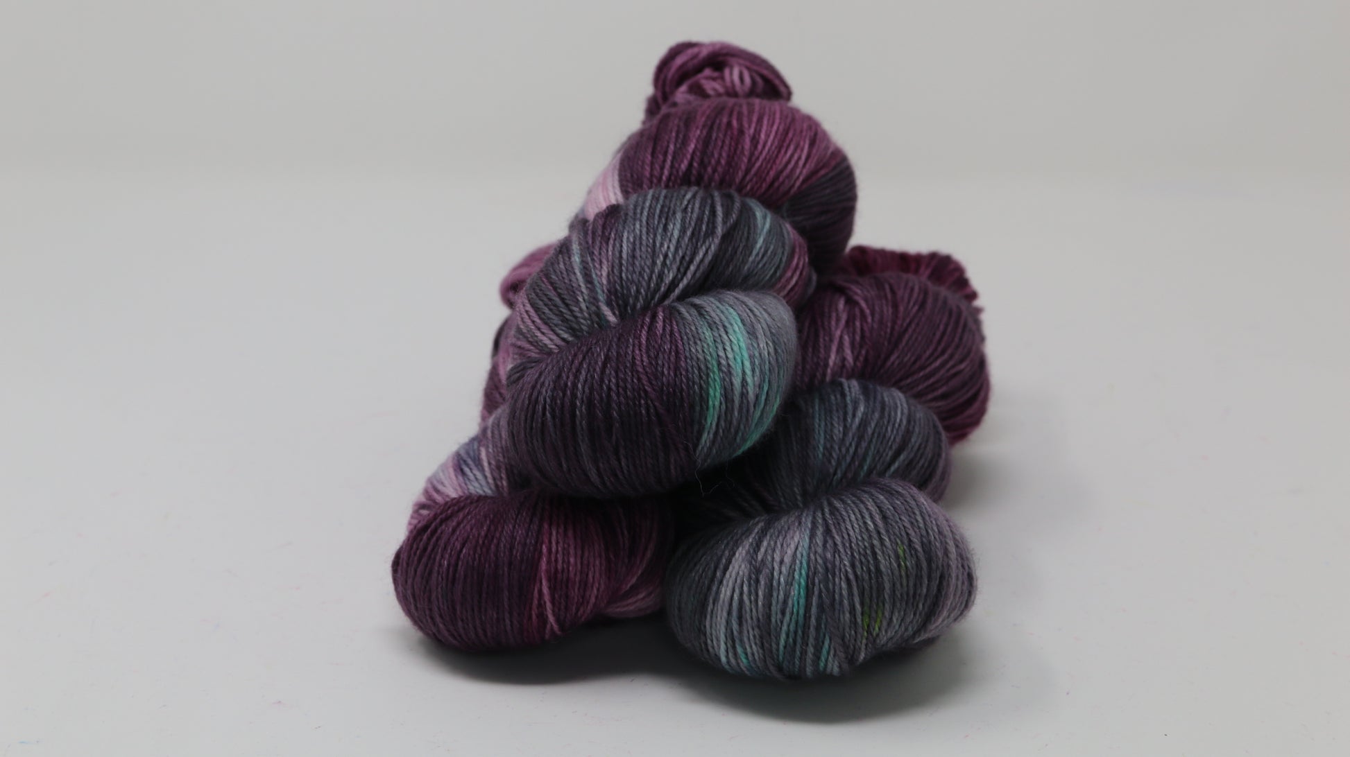 Three skeins of variegated yarn skeins in shades of purple, pink, green and dark gray