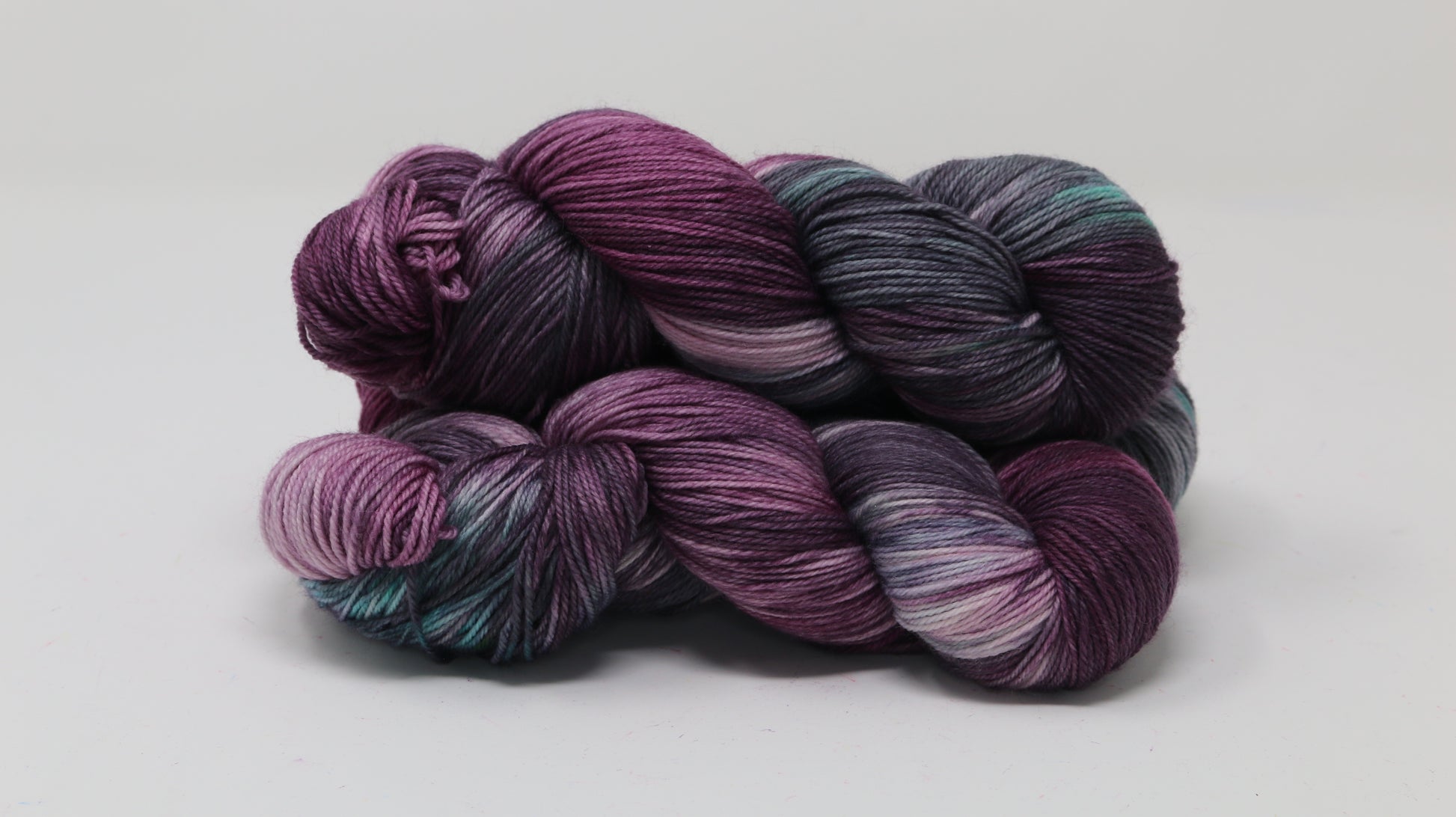Three skeins of variegated yarn skeins in shades of purple, pink, green and dark gray
