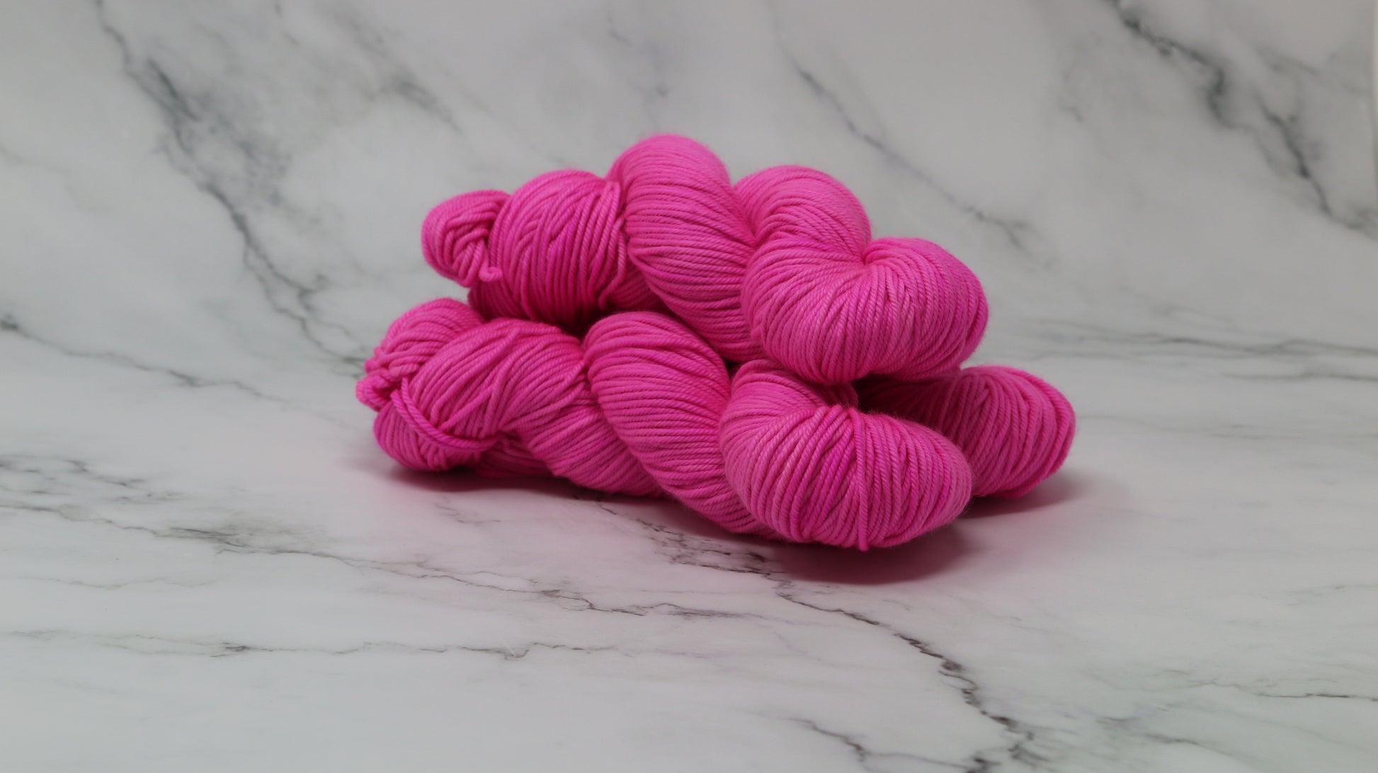 3 skeins of hot pink yarn displayed on a white marble surface and background