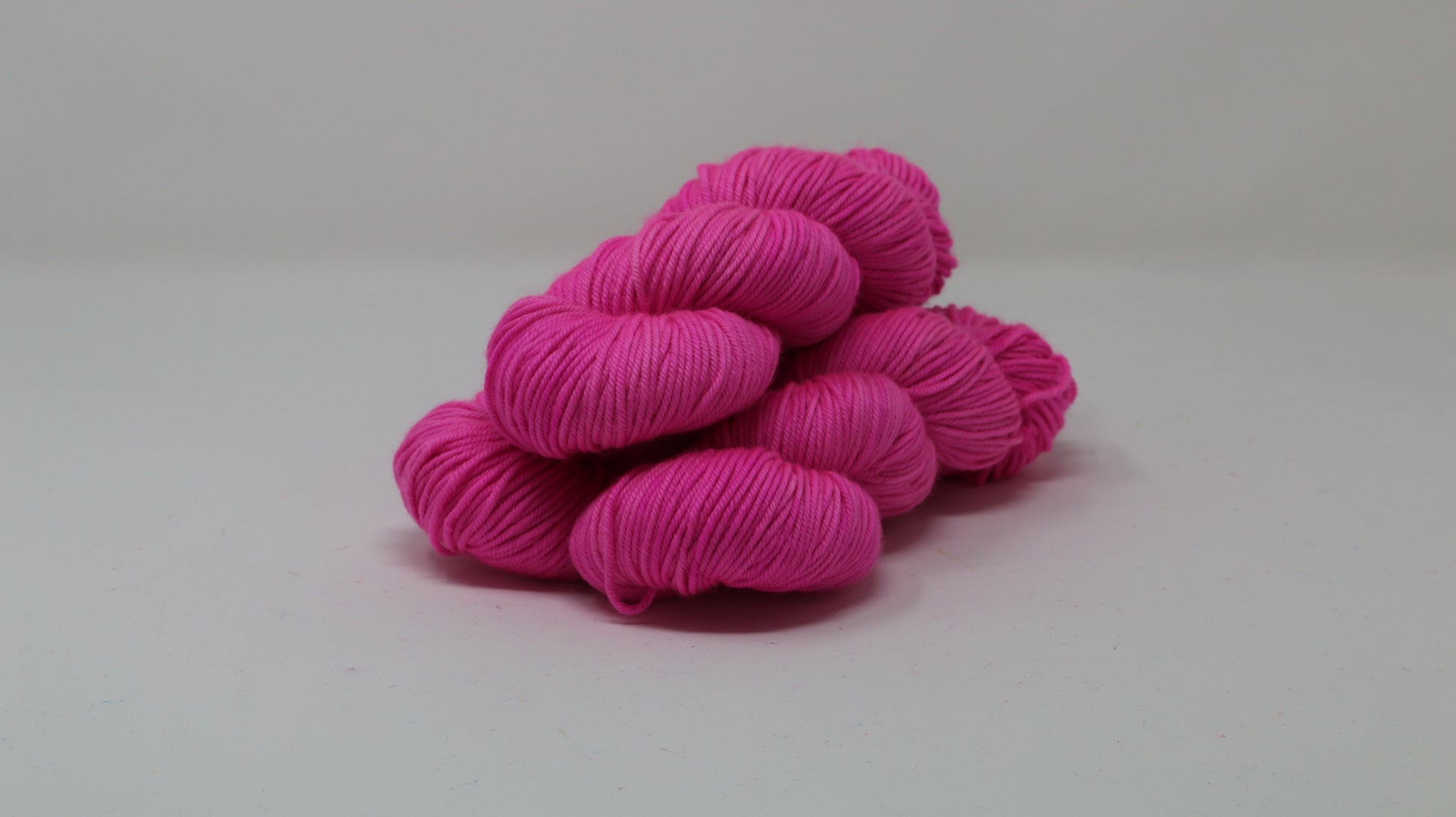 3 skeins of hot pink yarn displayed on a white surface and background