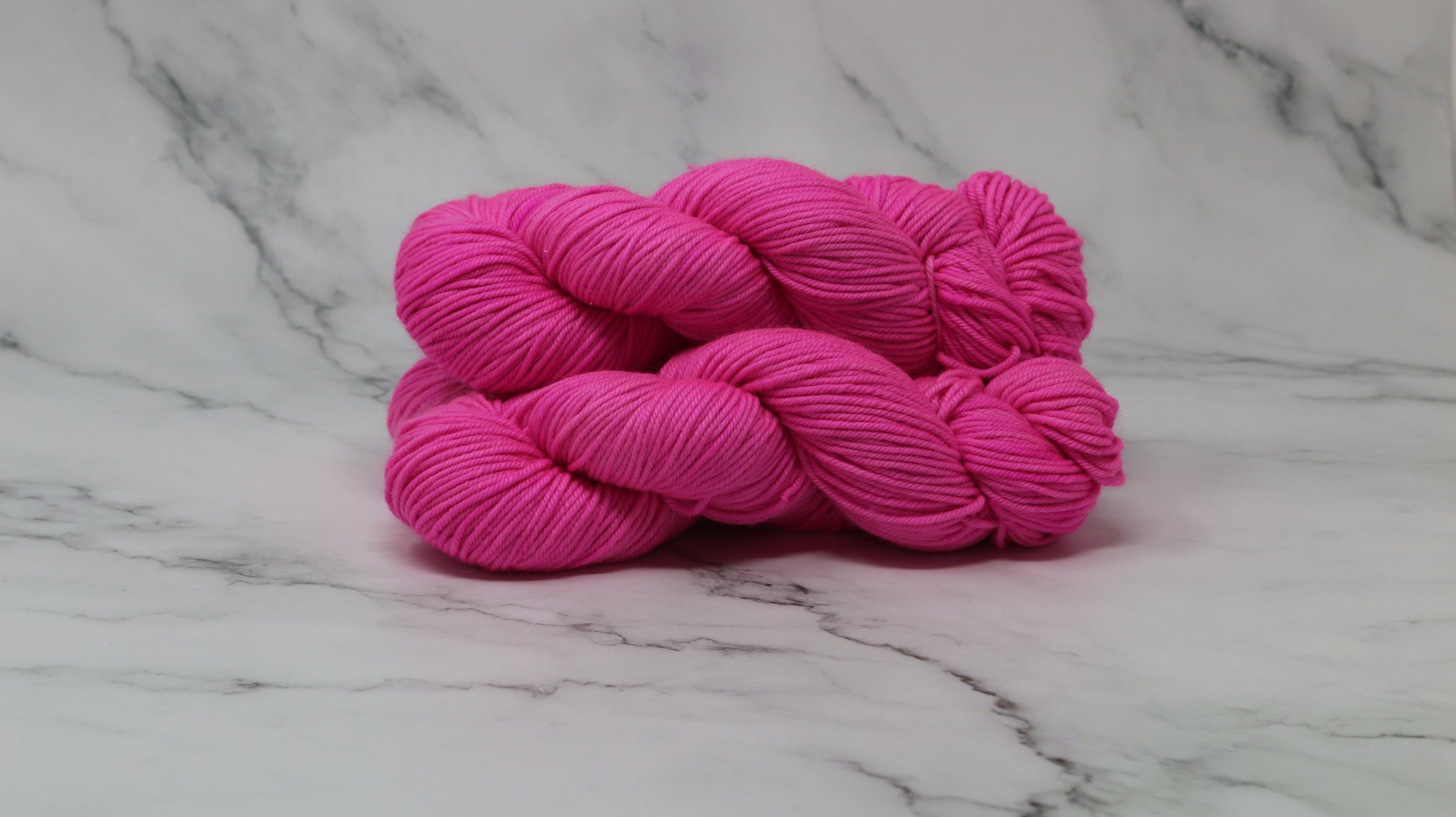 3 skeins of hot pink yarn displayed on a white marble surface and background