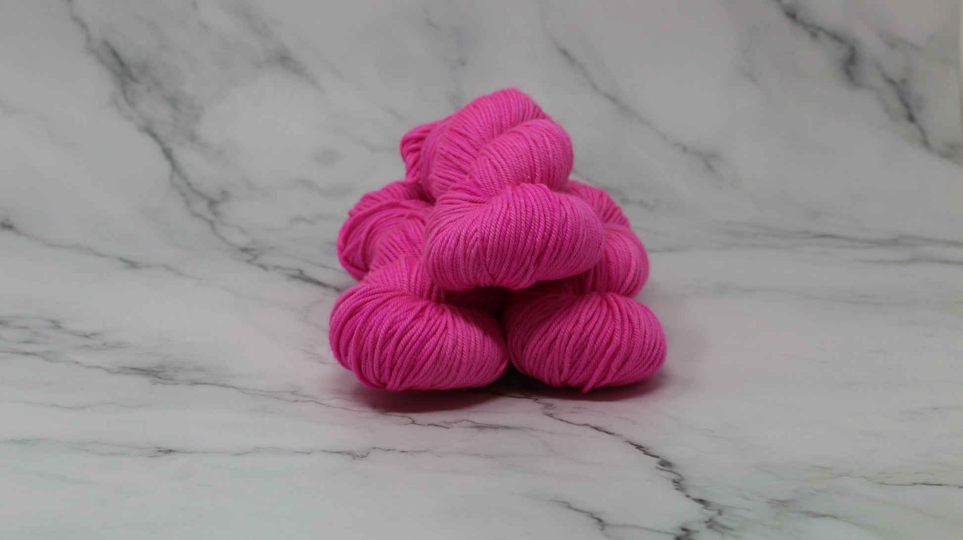 3 skeins of hot pink yarn displayed on a white marble surface and background
