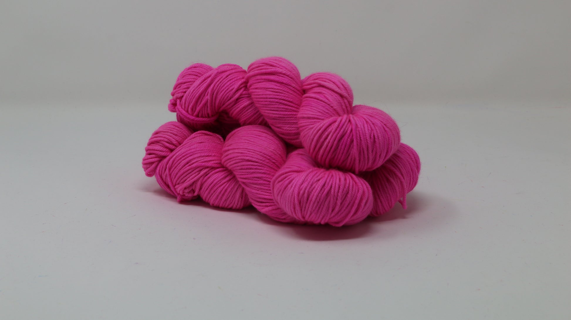 3 skeins of hot pink yarn displayed on a white surface and background