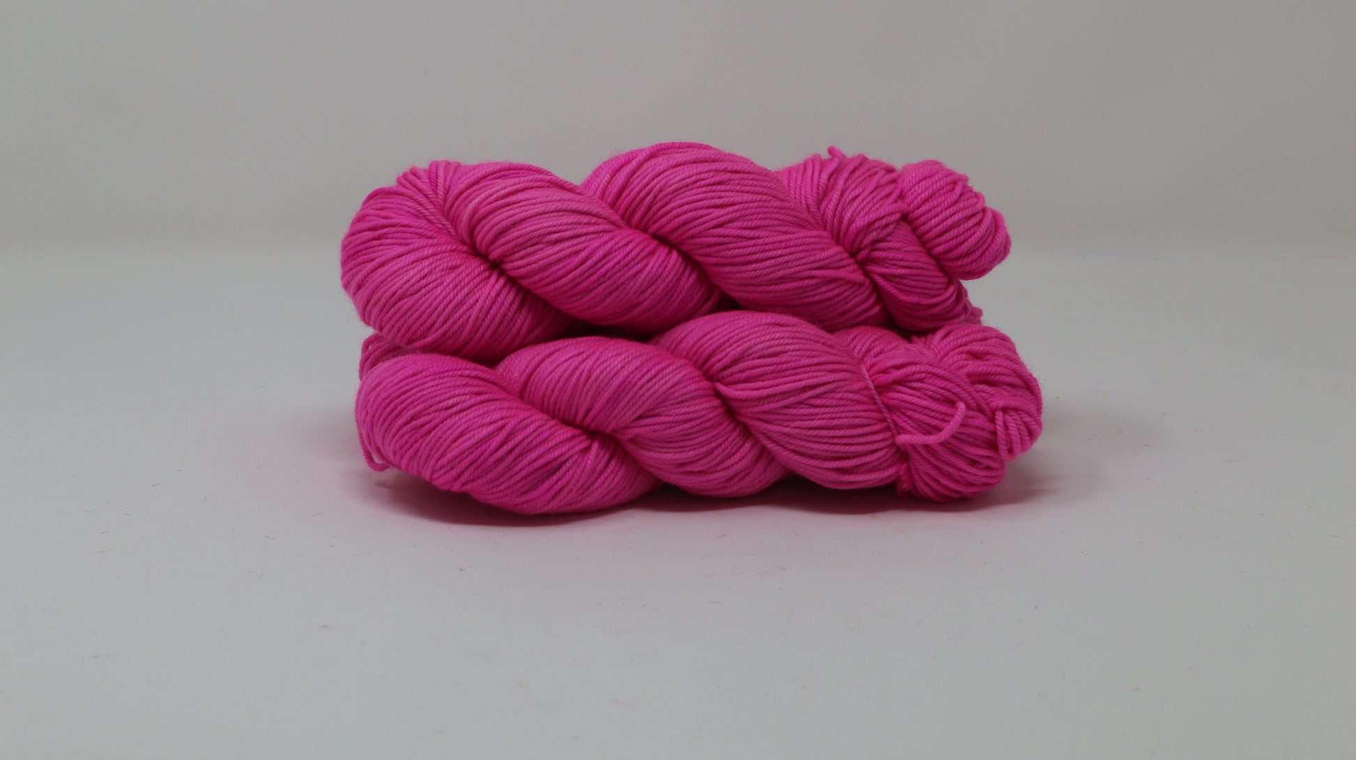 3 skeins of hot pink yarn displayed on a white surface and background