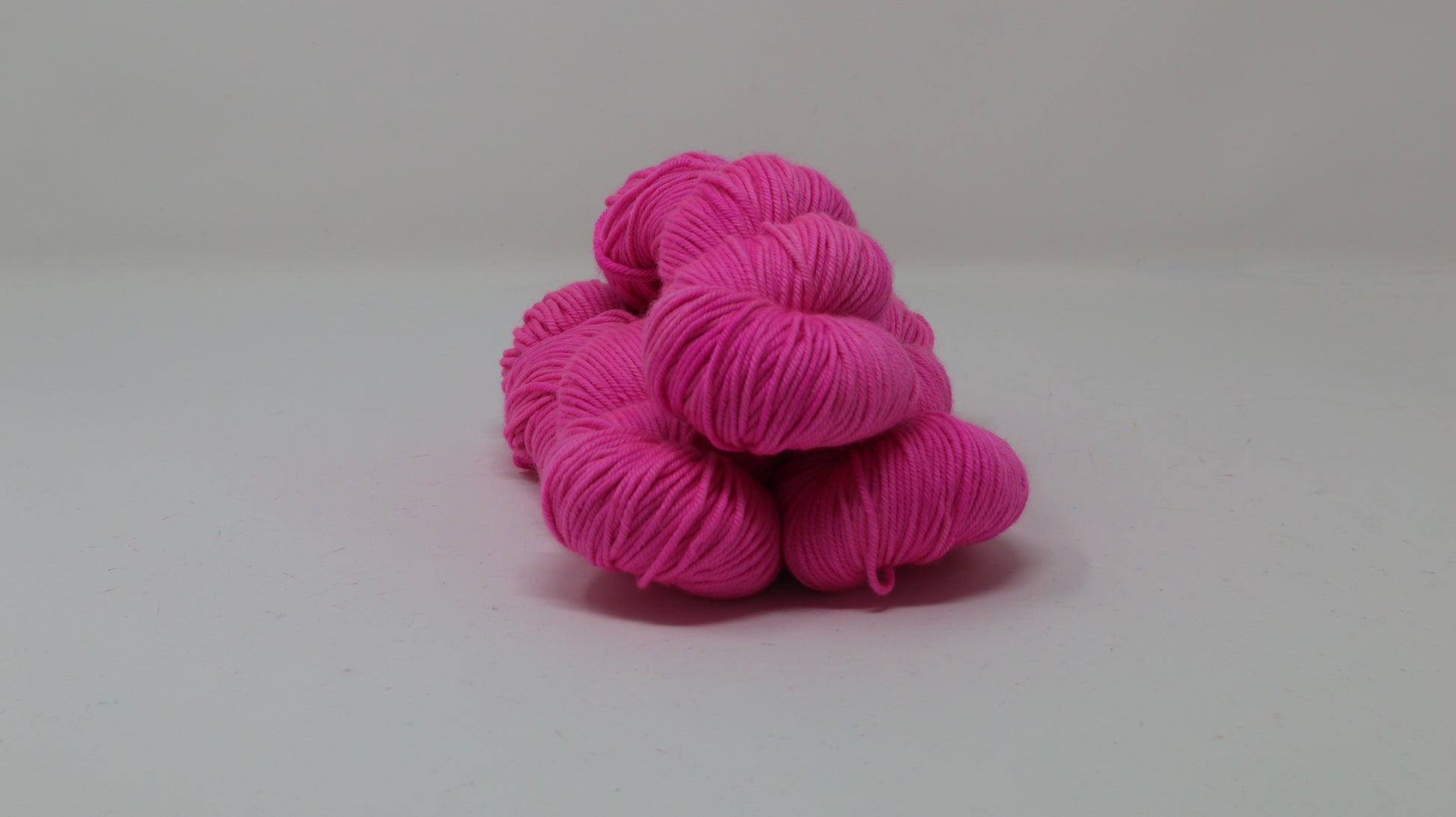 3 skeins of hot pink yarn displayed on a white surface and background