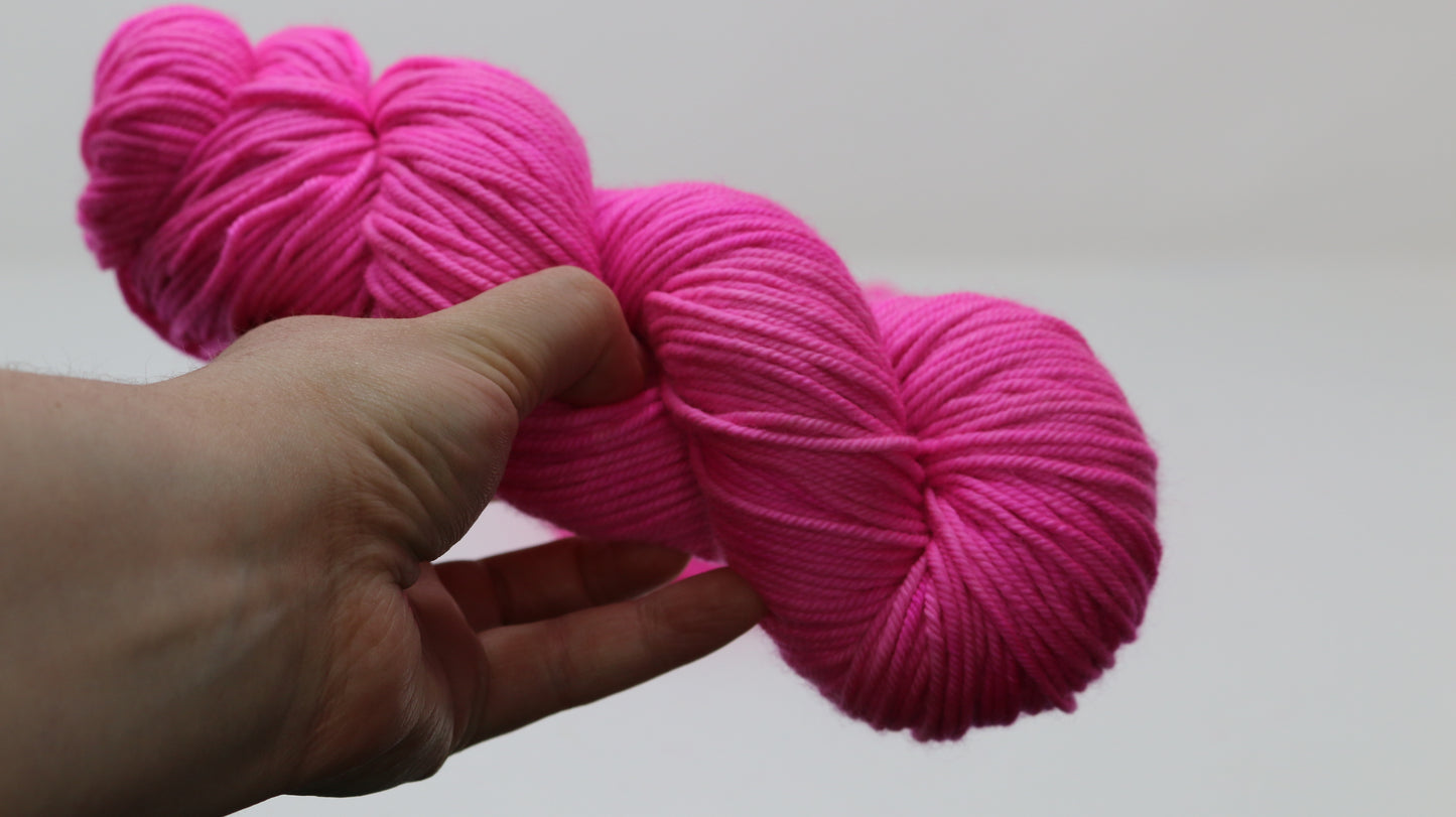 A skein of hot pink yarn held in a person's left hand in front of a white background