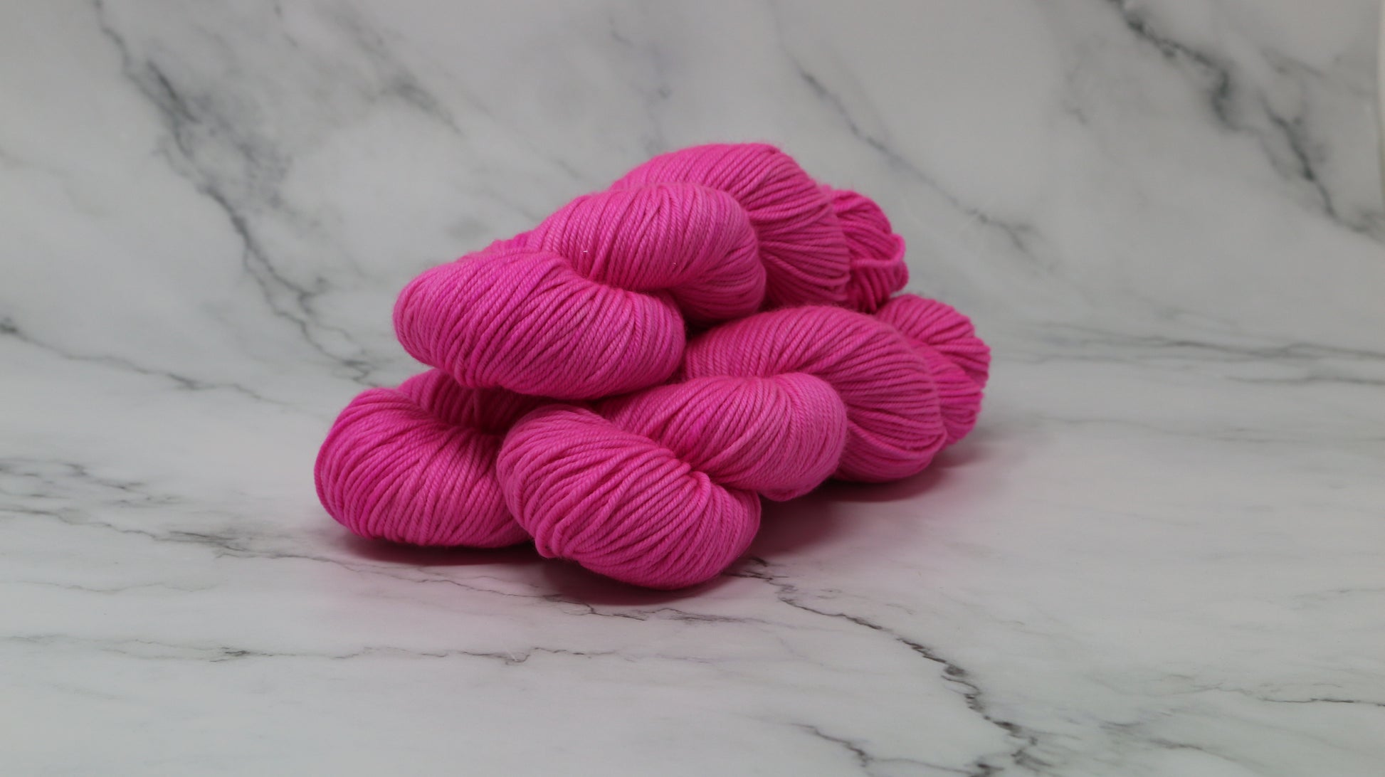 3 skeins of hot pink yarn displayed on a white marble surface and background