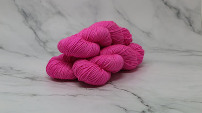 3 skeins of hot pink yarn displayed on a white marble surface and background