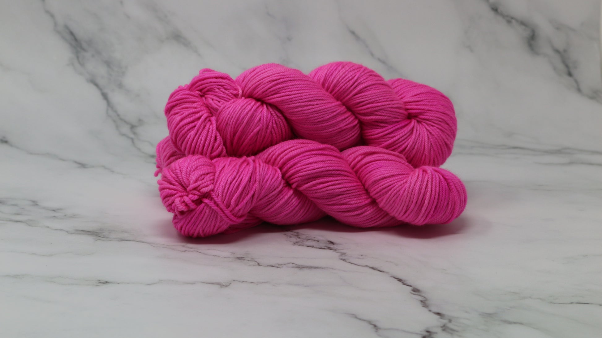 3 skeins of hot pink yarn displayed on a white marble surface and background