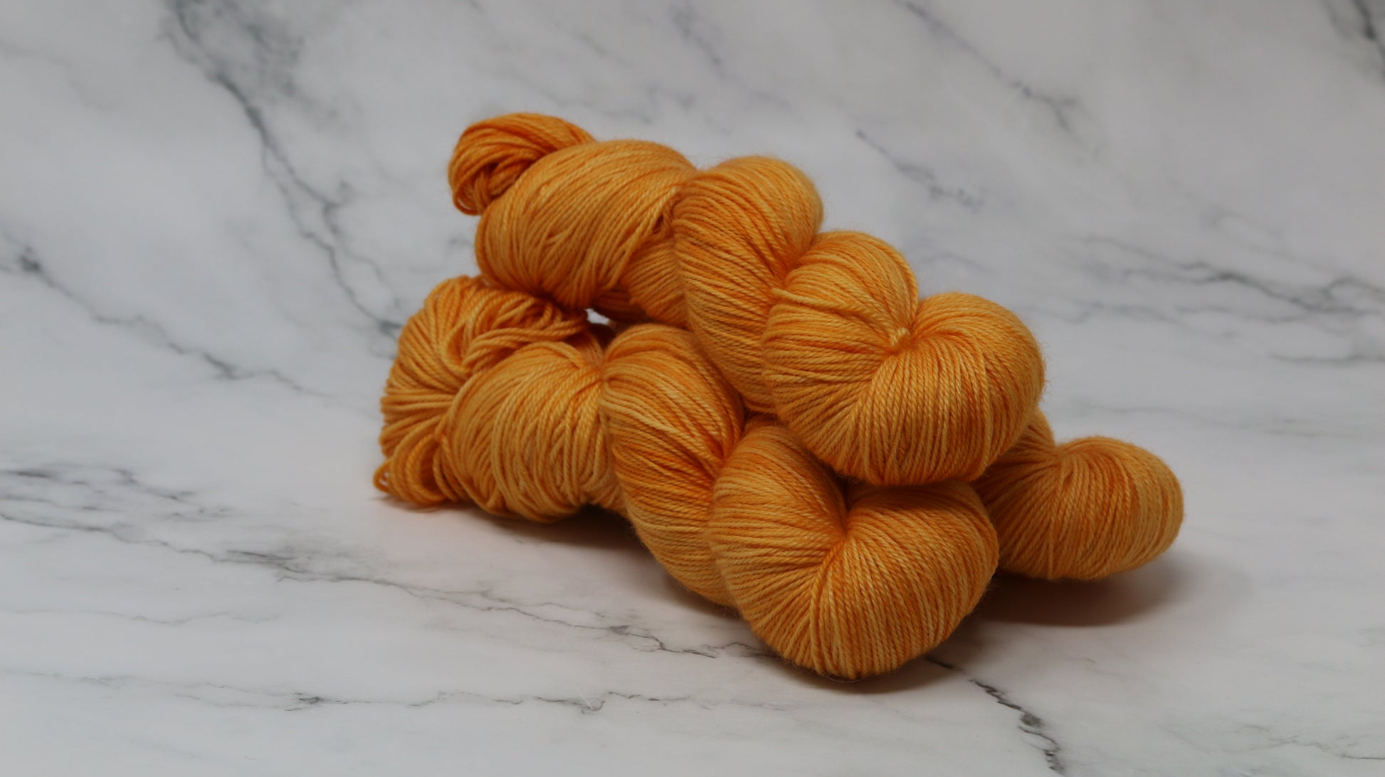 3 skeins of orange yarn on a white marble surface and background