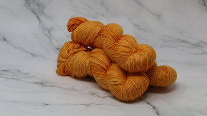 3 skeins of orange yarn on a white marble surface and background