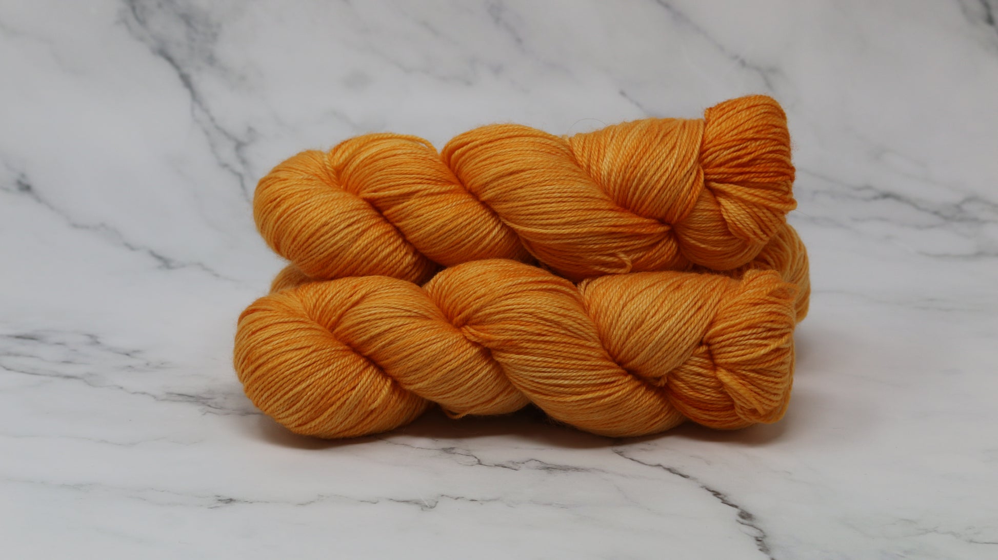 3 skeins of orange yarn on a white marble surface and background