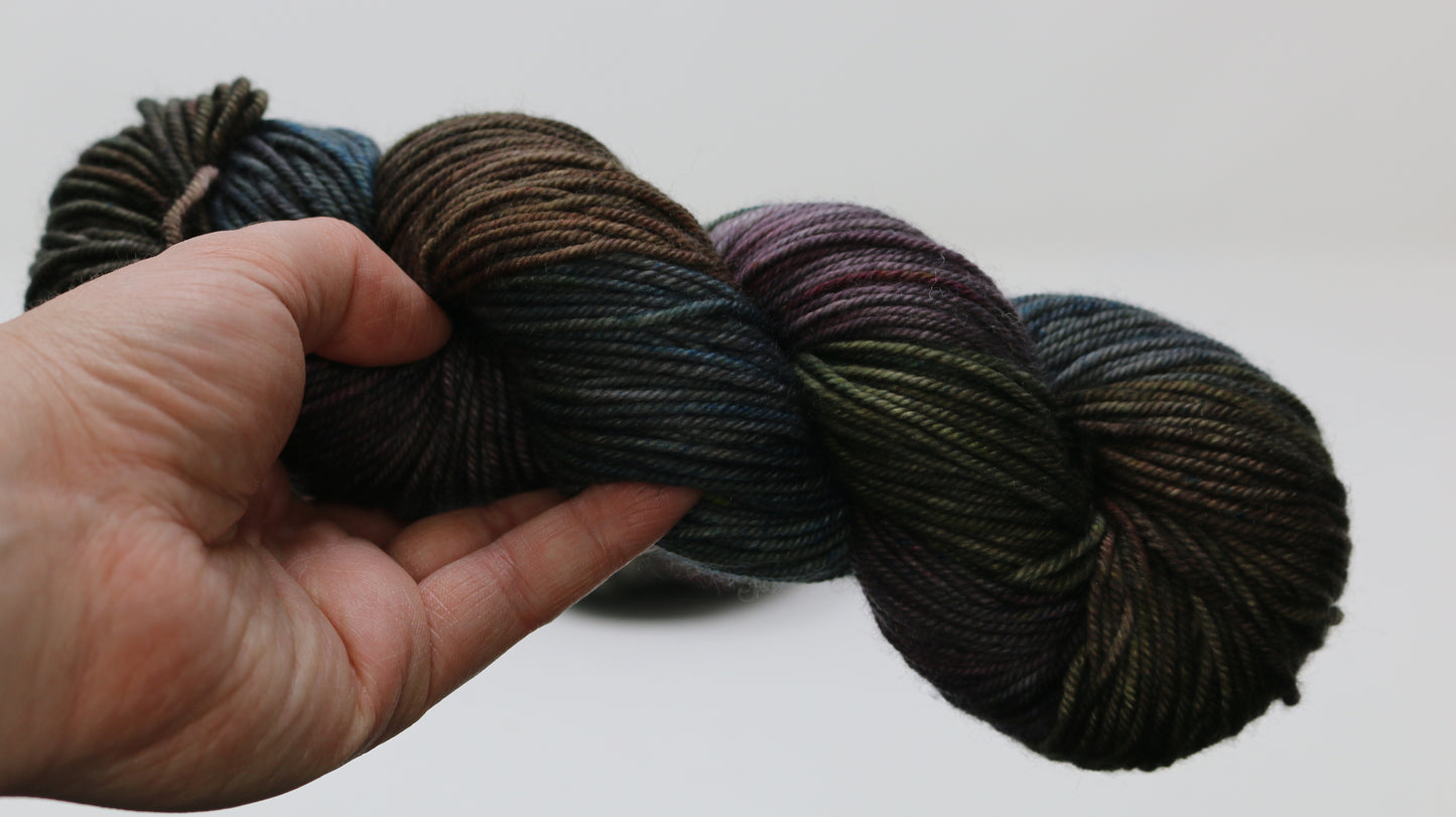 A skein of multi coloured yarn held by a person's left hand in front of a white background